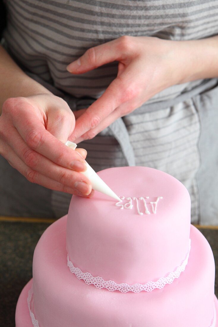 Letters being iced onto a three-tier cake from a piping bag