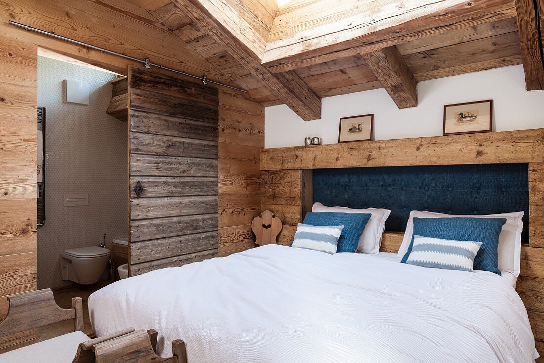 Double bed with rustic headboard in attic bedroom with ensuite bathroom