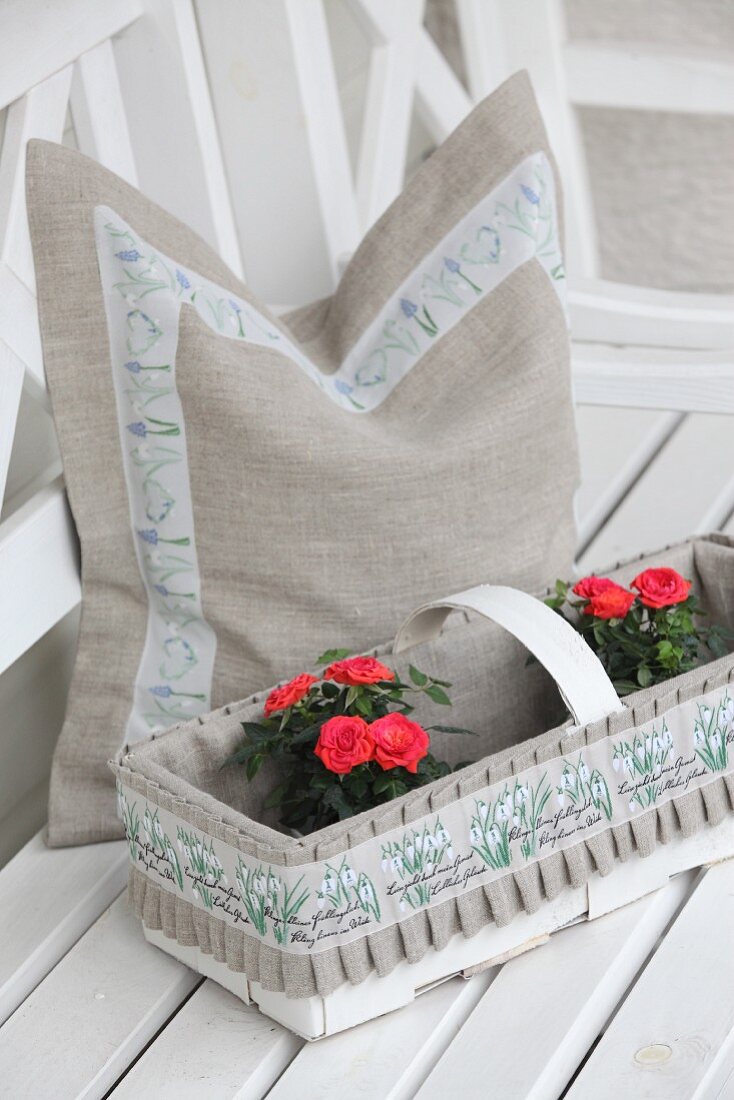 Cushion cover hand made from undyed linen with floral trim behind roses in decorated chip wood basket