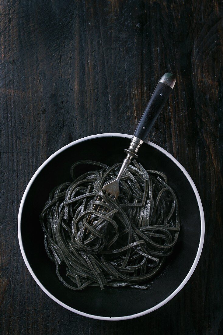 Gekochte Tintenfischspaghetti auf schwarzem Hintergrund
