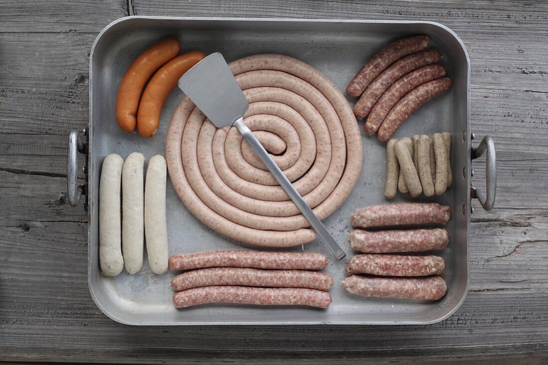 Various types of fresh sausage in a metal roasting tray