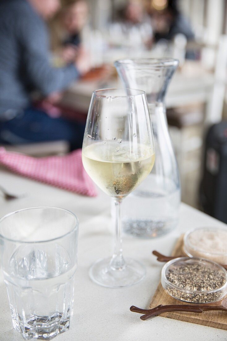 A glass of white wine with water, salt and pepper on a table in a restaurant