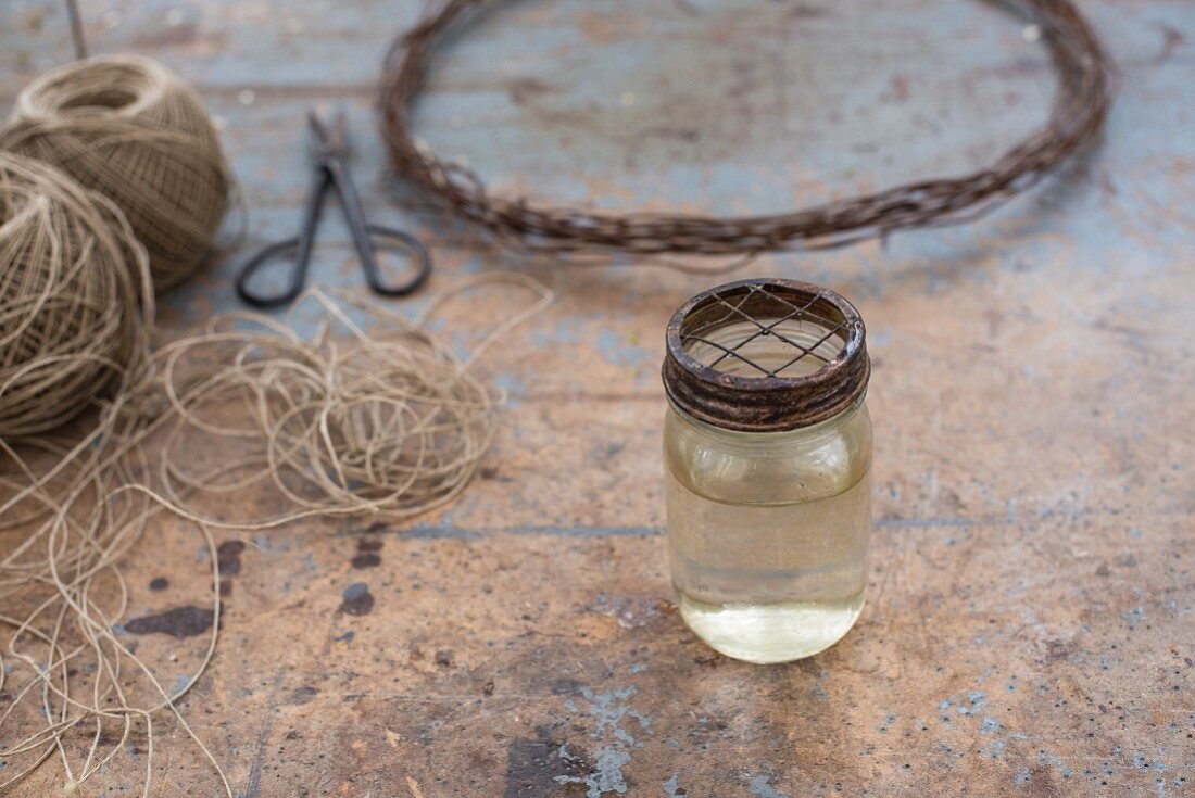 Glas mit Flüssigkeit und Metalldeckel vor Paketschnur und Drahtkranz