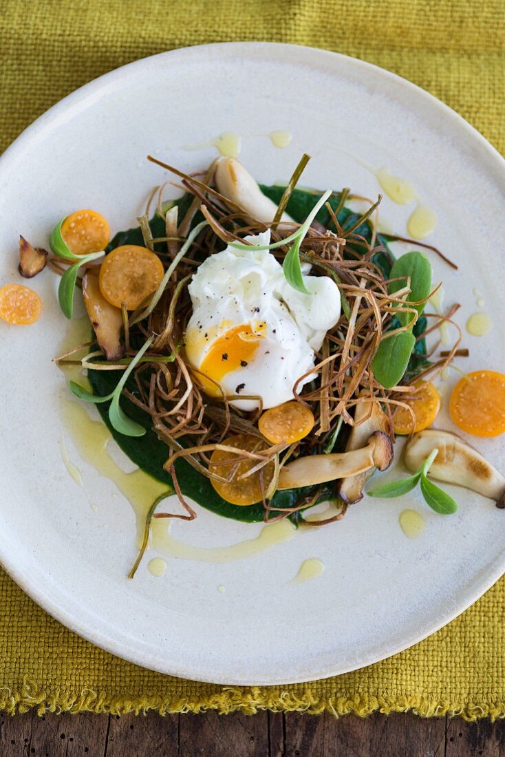 A poached egg on fried leeks with spinach puree, herbs, kumquats and borage shoots