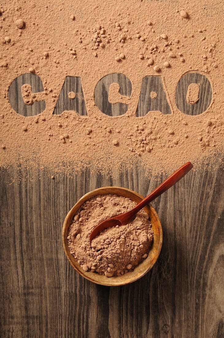 Cocoa powder in a bowl and spilled on a wooden background with the word 'cacao'
