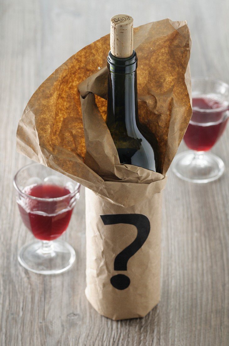 A bottle of red wine in a paper bag with a question mark