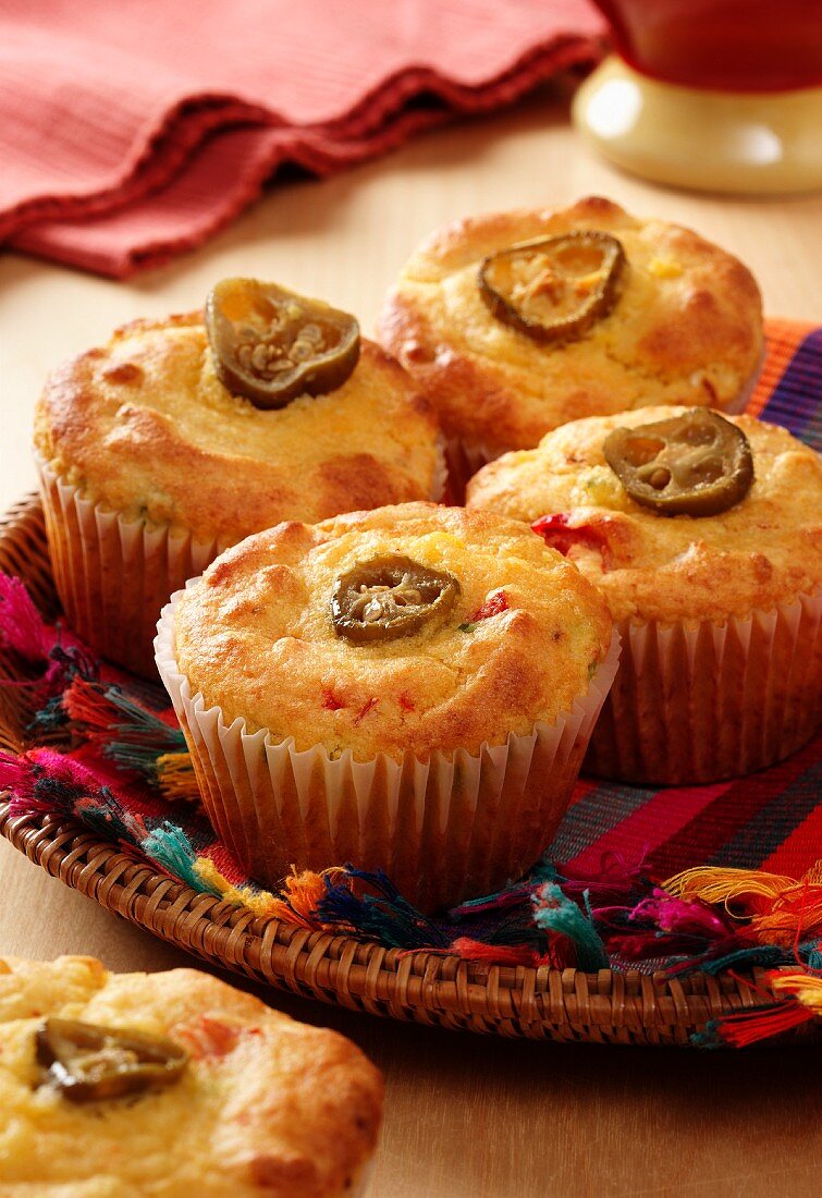 Mexican corn bread muffins on a multi coloured cloth in a flat backet on a wooden surface