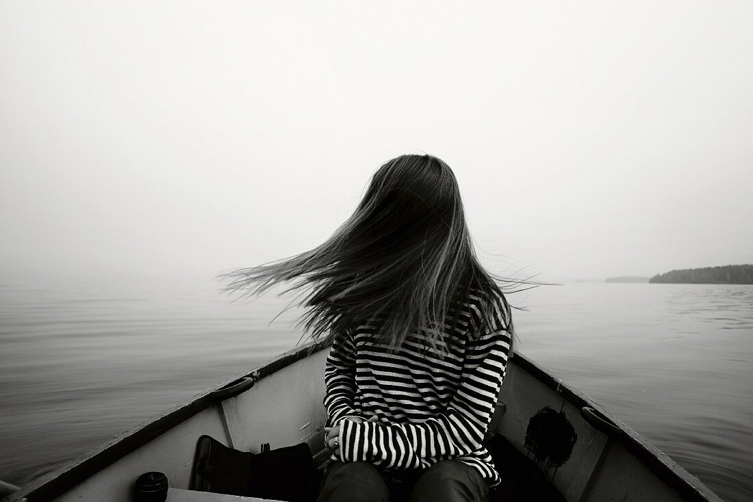 Junges Mädchen in Ringelshirt sitzt in einem Boot und wirft ihre Haare zur Seite (s/w-Bild)