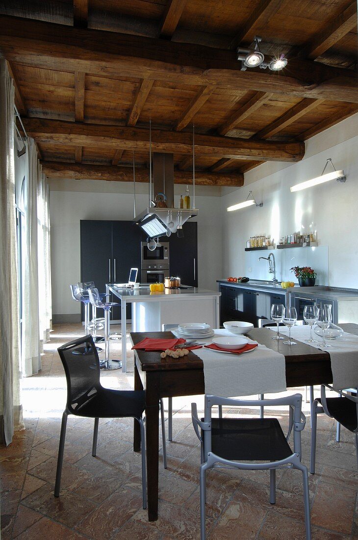 Modern, open-plan kitchen below rustic wood-beamed ceiling
