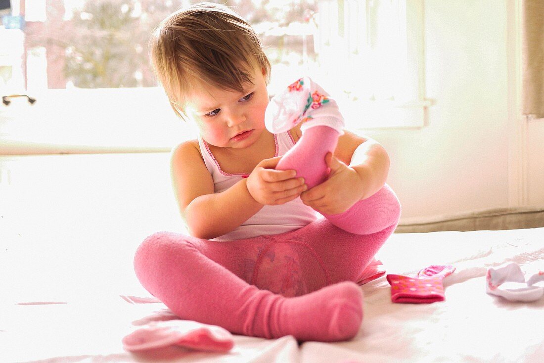 A little girl wearing pink putting socks on