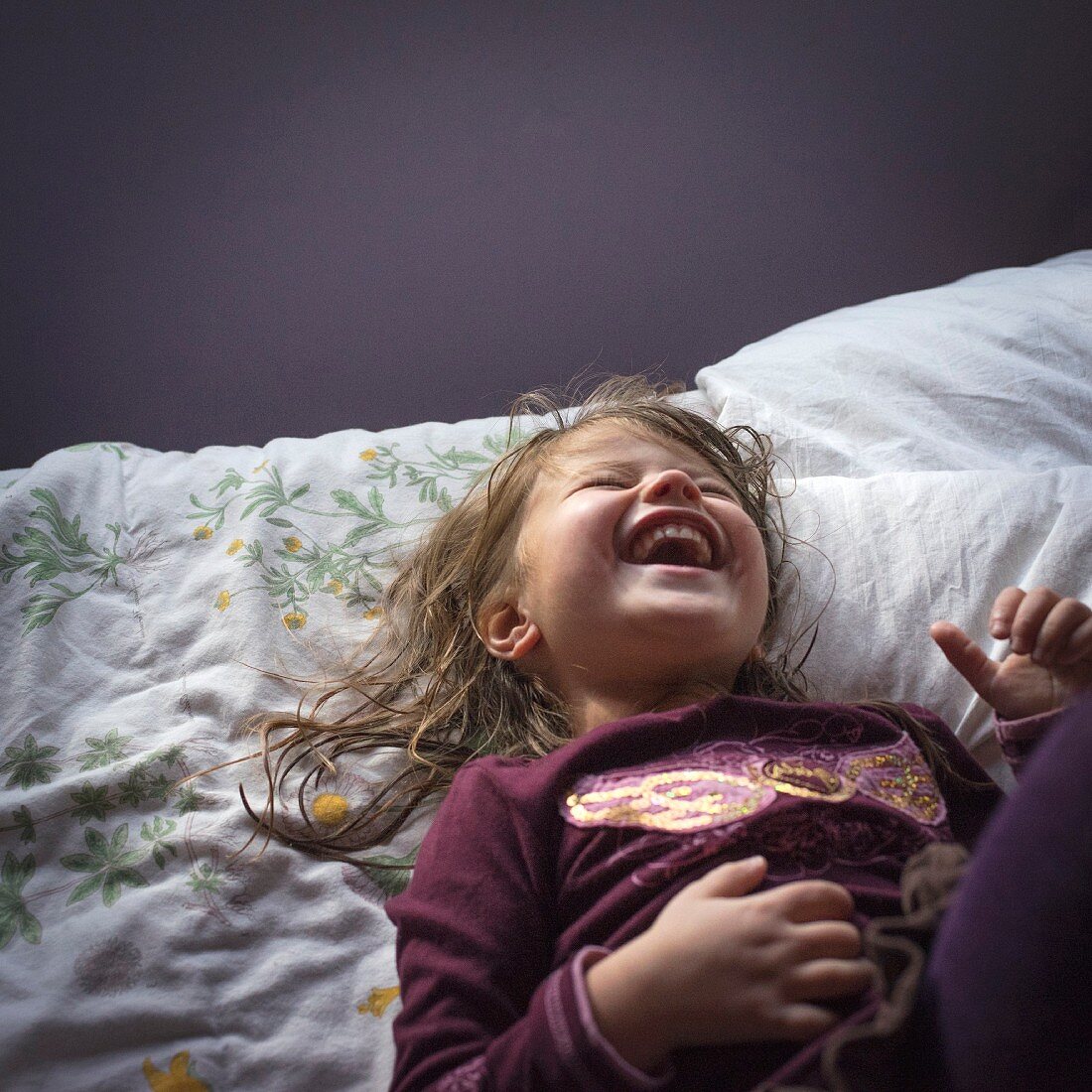A laughing little girl in pyjamas lying on a bed