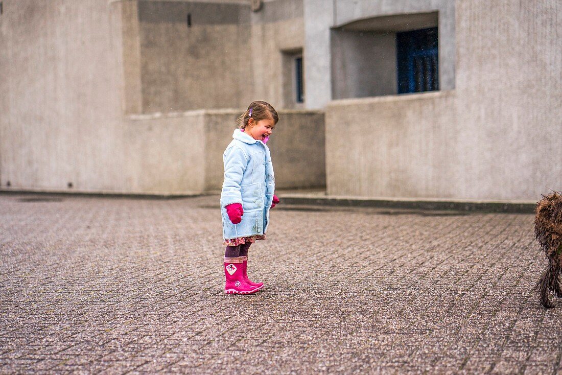 A laughing little girl wearing winter clothing standing in a street