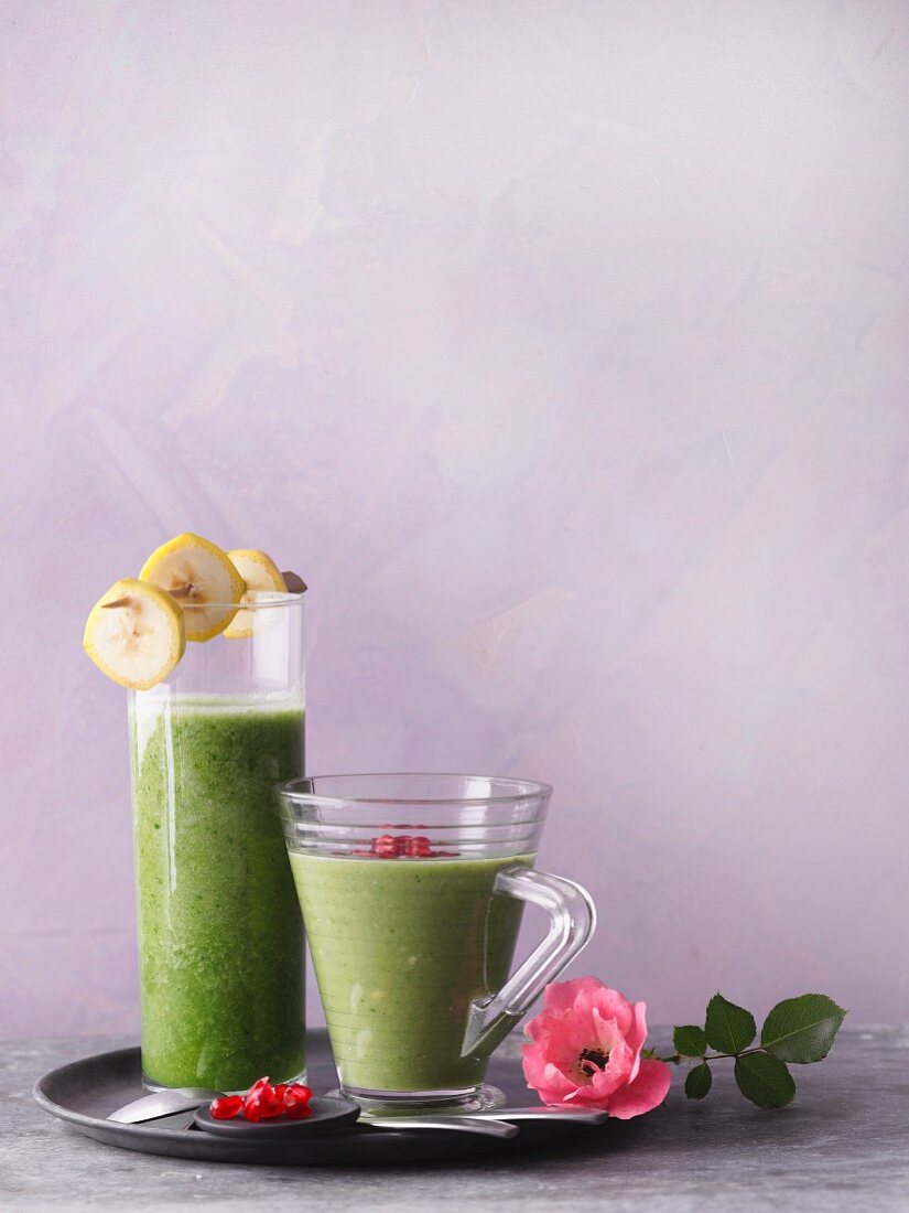 Two green smoothies garnished with pomegranate seeds and banana