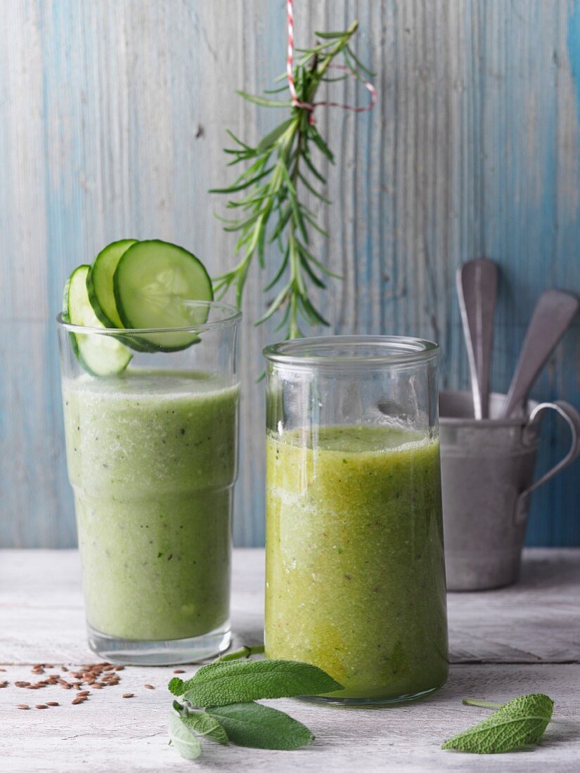 Two green smoothies garnished with cucumber and herbs