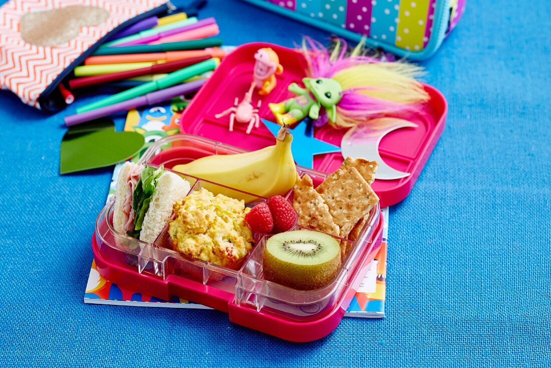 Pausenbox mit Banane, Kiwi, Gemüsemuffin, Sandwich und Himbeeren