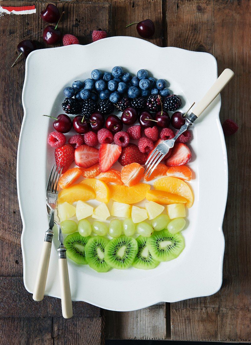 Fruit salad arranged in rainbow stripes on a serving platter