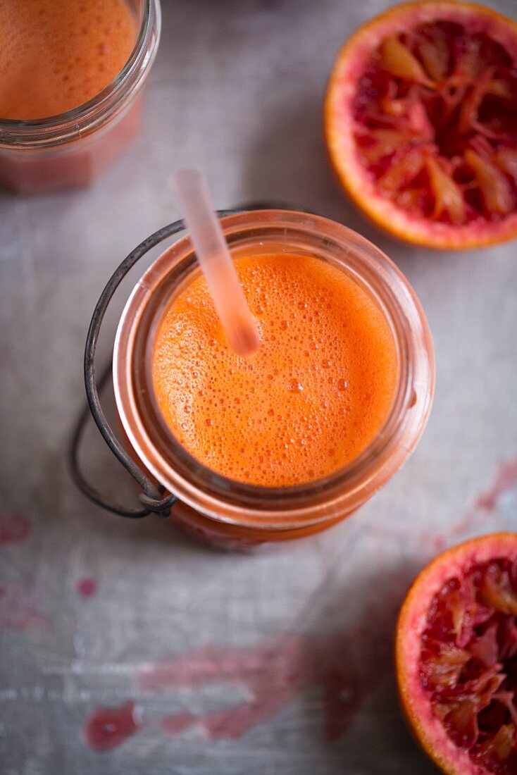 Blood orange smoothie in a glass jar with a straw