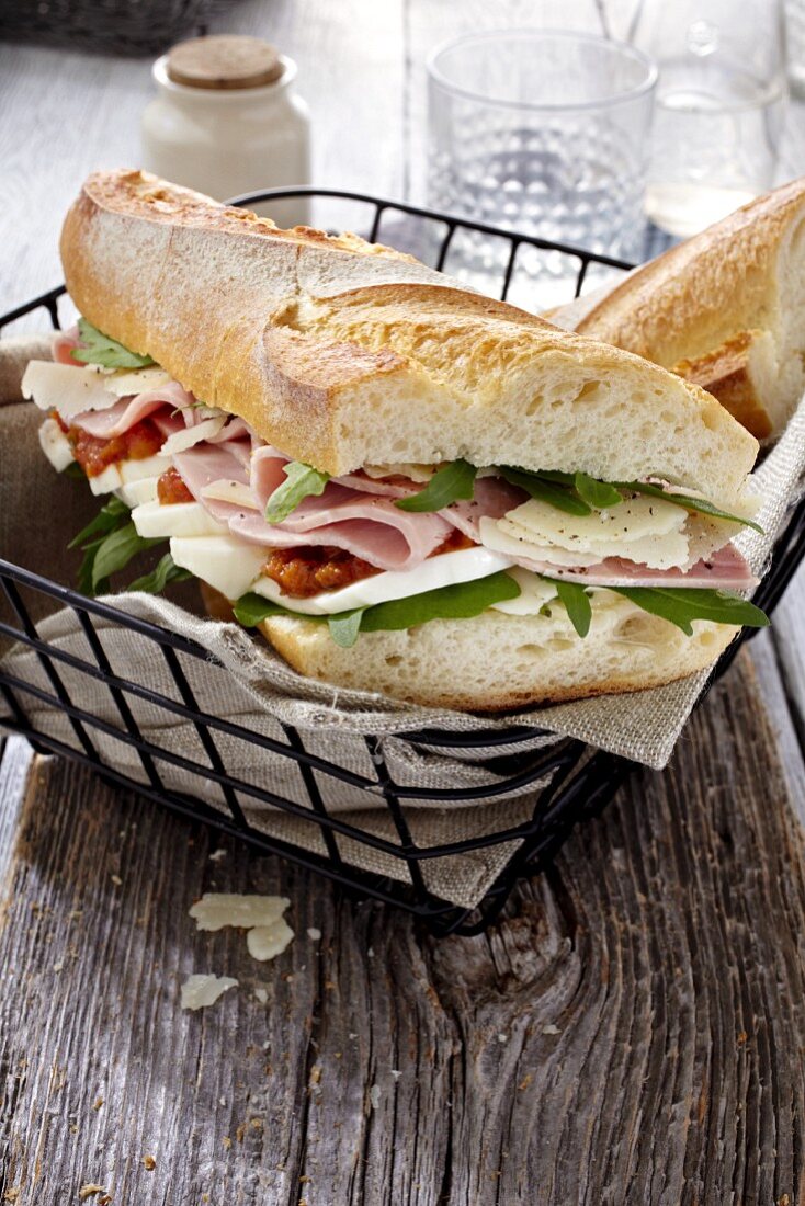 A baguette sandwich with ham, tomatoes, basil and rocket