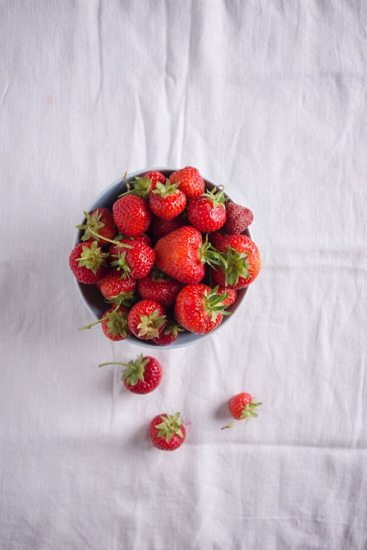 A bowl of fresh strawberries on a white tablecloth