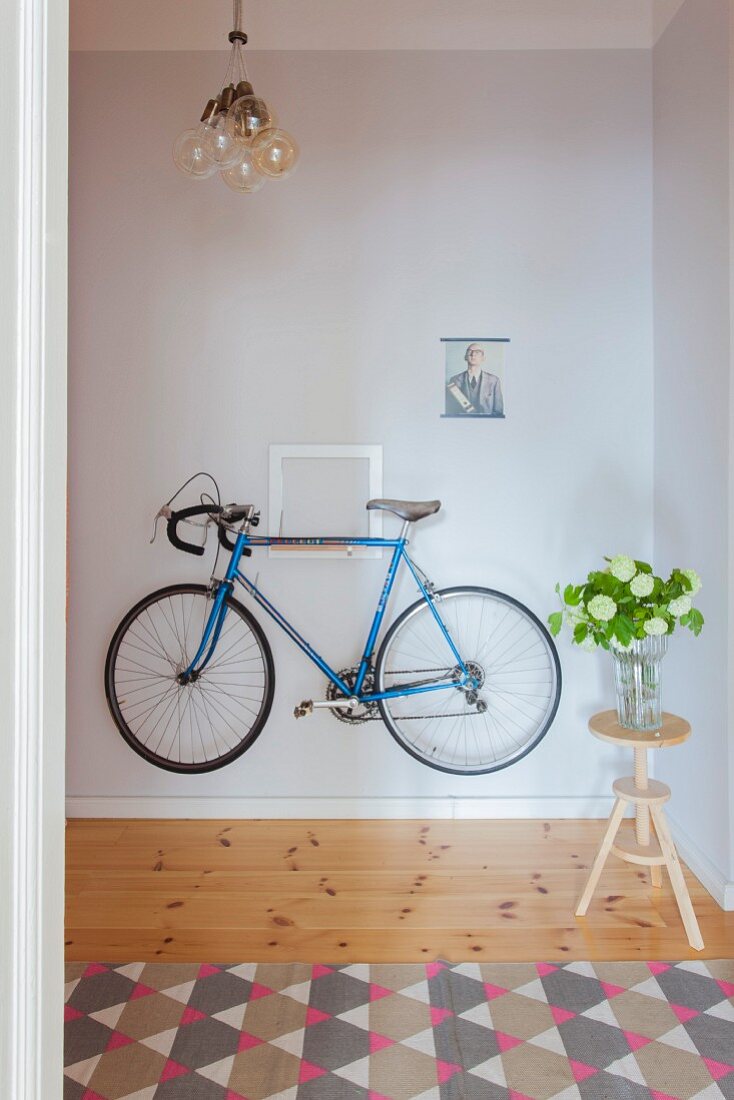Blaues Fahrrad hängt an der Wand im Flur, Blumen auf einem Hocker