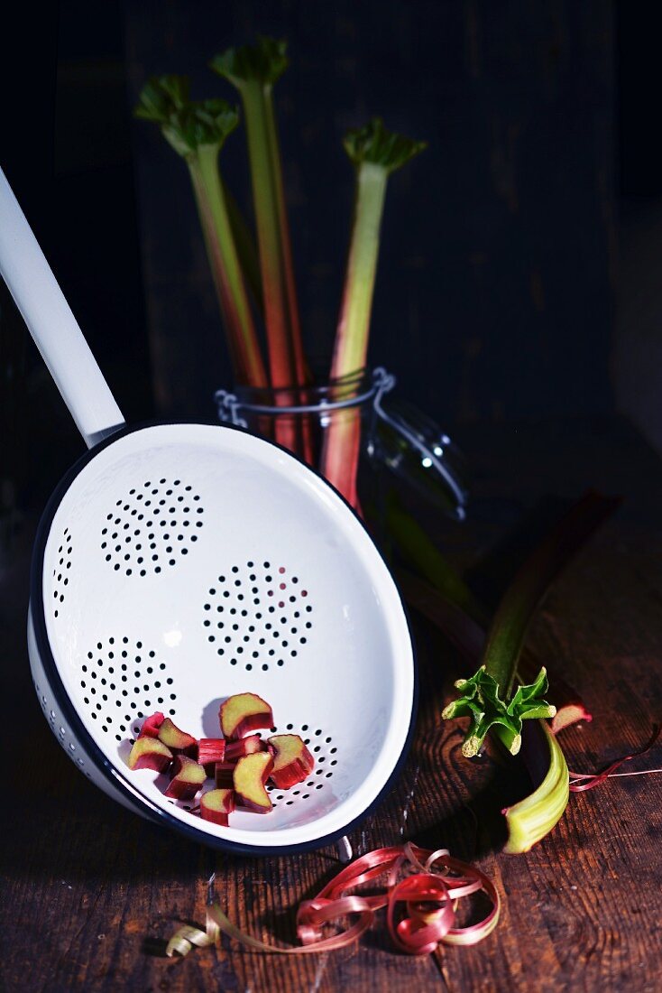 Pieces of rhubarb in a colander and a glass next to peeled rhubarb stems