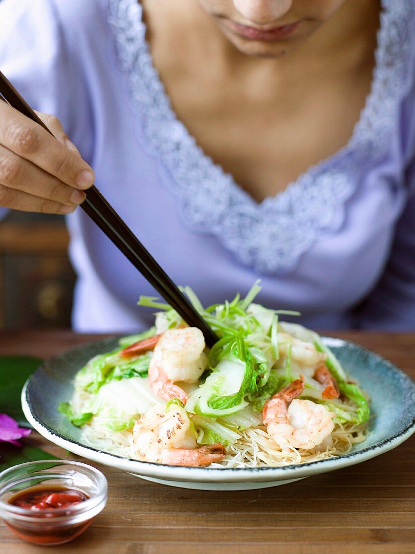 Frau isst gebratene Reisnudeln mit Garnelen und Chinakohl