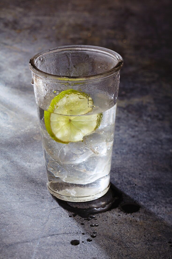Ein Glas Wasser mit Eiswürfeln und Limettenscheibe