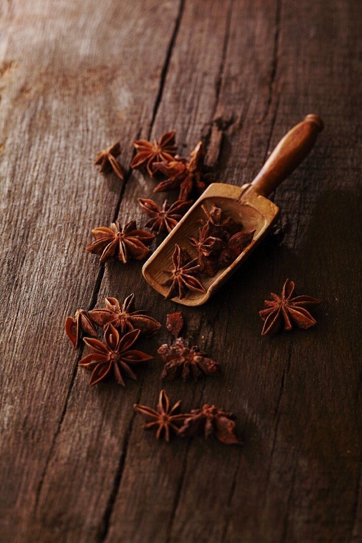 Star anise on a rustic wooden table with a small wooden scoop