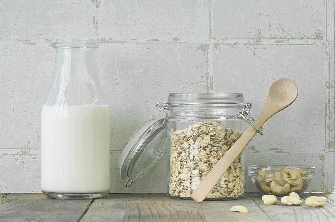 Muesli ingredients: oat in a storage jar, a bottle of milk and cashew nuts