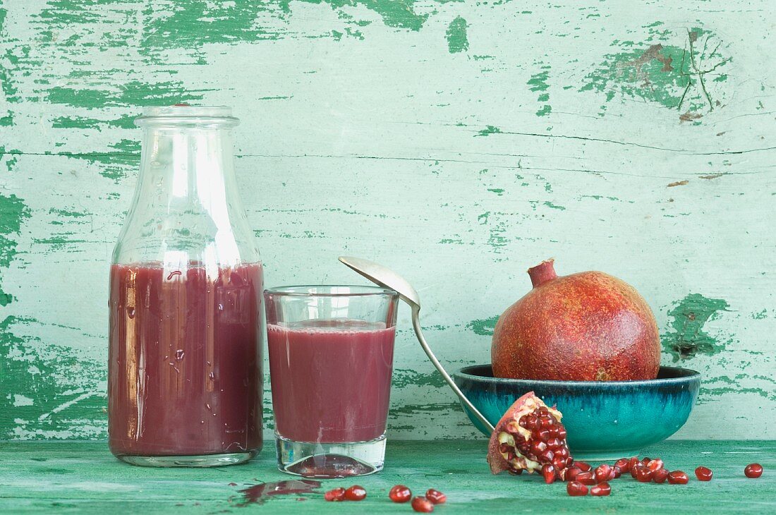 An arrangement of pomegranates and pomegranate juice in a bottle and a glass