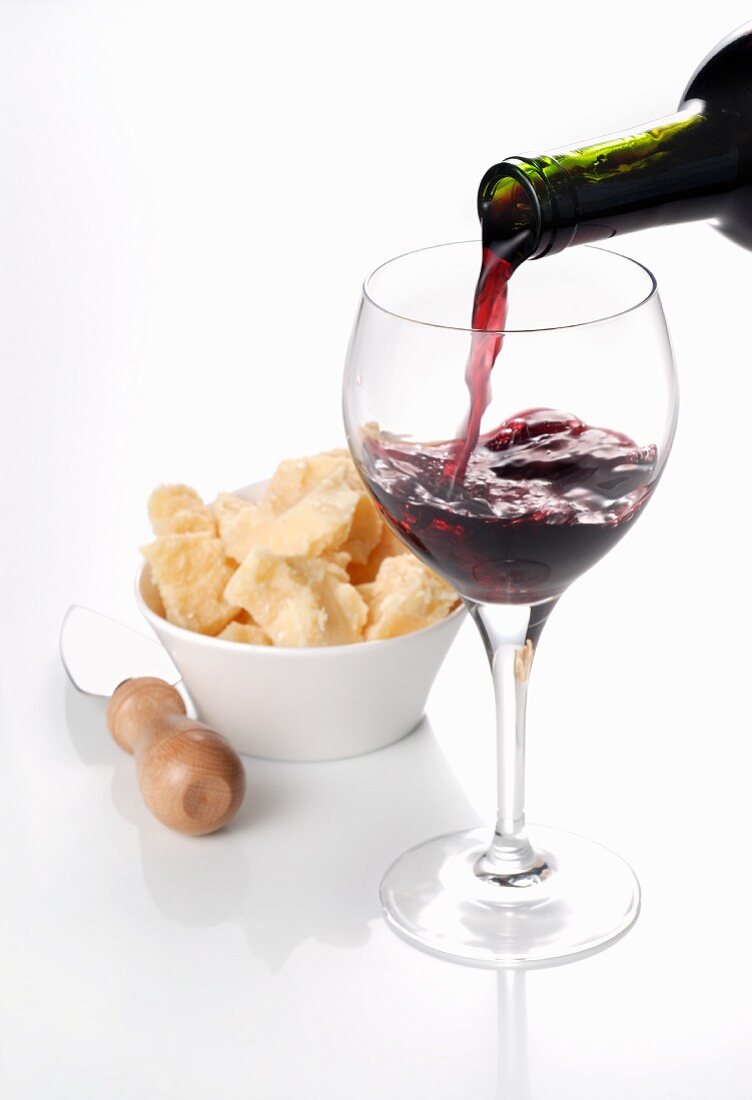 Red wine being poured into a glass with a bowl of Parmesan cheese in the background