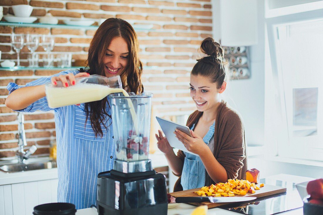 Zwei junge Frauen beim Zubereiten eines Smoothies mit Früchten