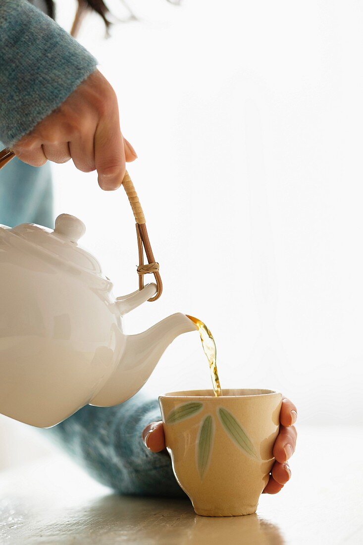 A woman pouring tea from an oriental teapot into a tea mug