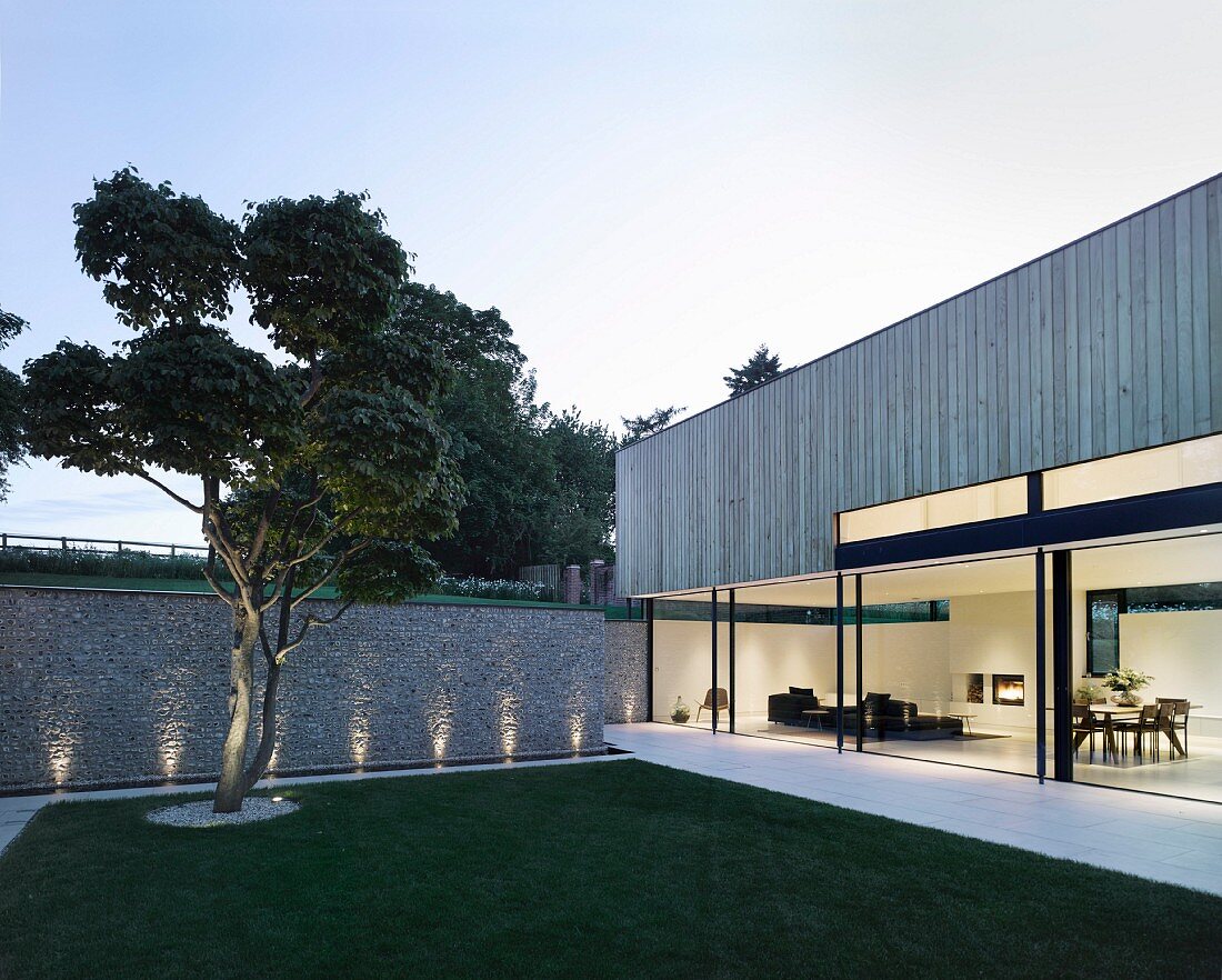 Detail of cubist façade with glass wall and wood cladding; view into living area