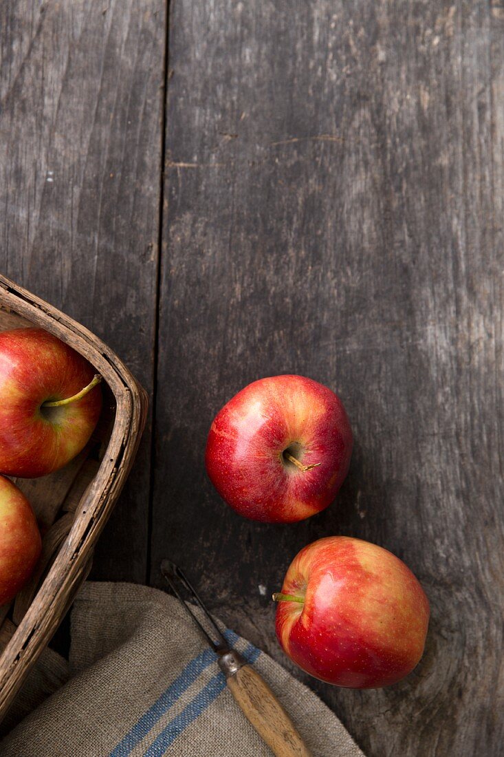 Red apples on a wooden board with a peeler and a basket