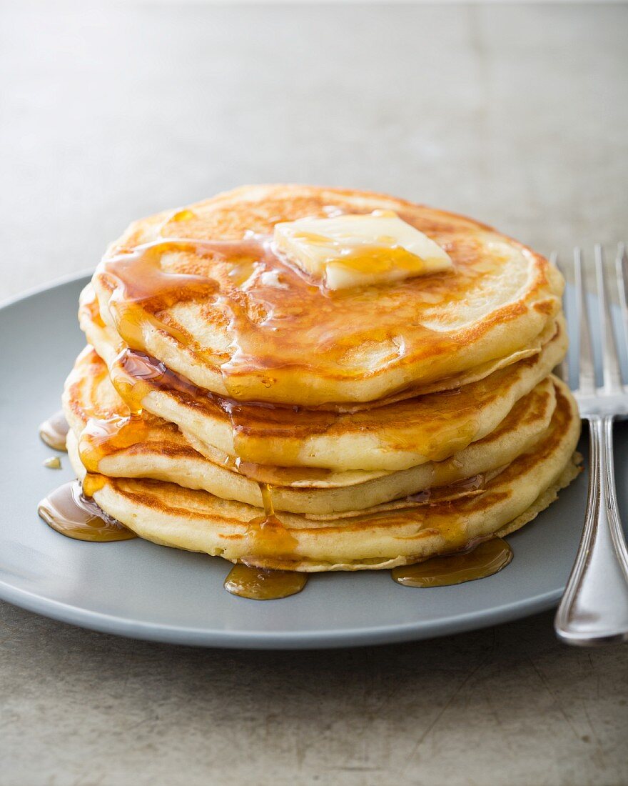 A stack of buttermilk pancakes on a plate with butter and maple syrup