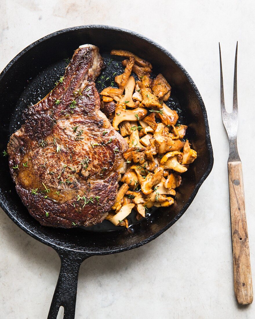 Ribeye steak in a cast-iron pan with sautéed mushrooms