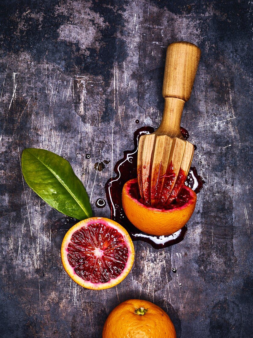 Blood oranges and a wooden citrus press on a metal surface