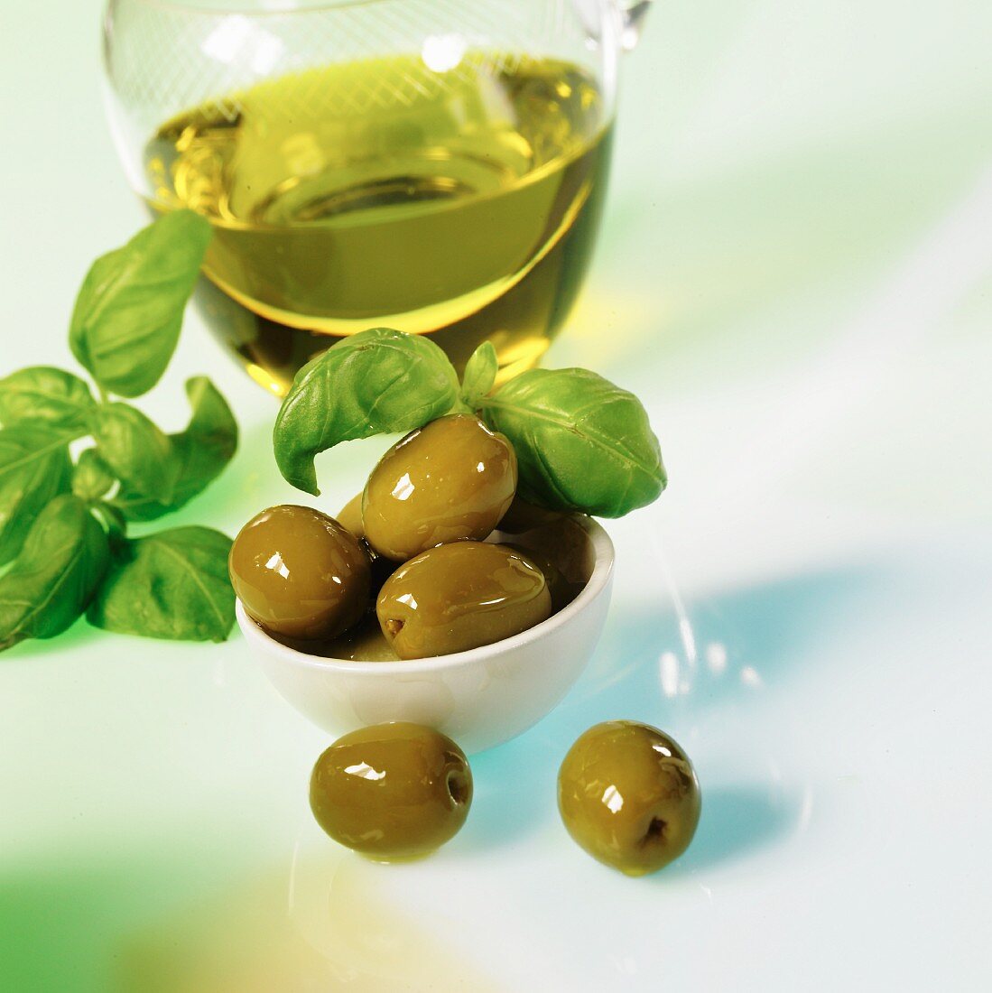 Green olives with olive oil and basil on a white surface