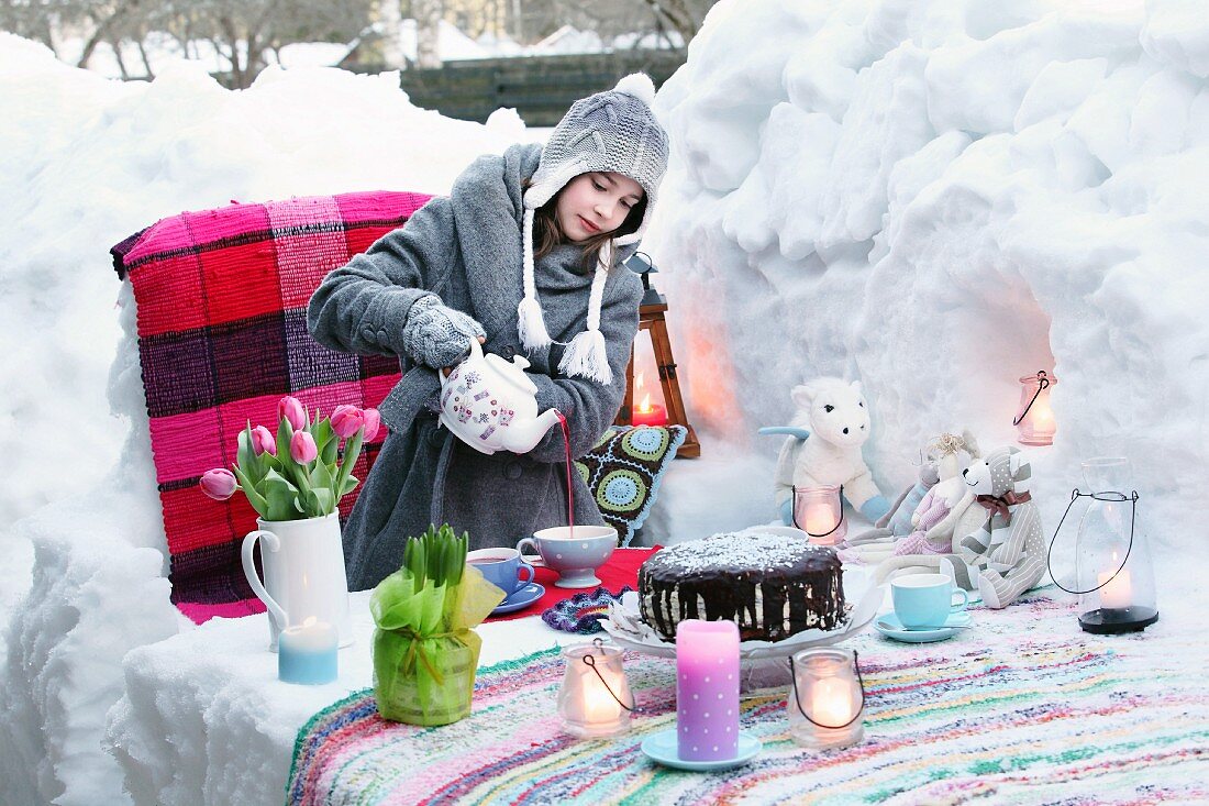 Mädchen beim Tee einschenken an Geburtstagstisch mit Windlichtern, Kuchen und Tulpenstrauss