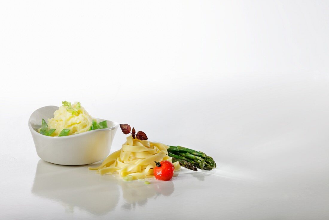 Tagliatelle with sautéed cherry tomatoes, basil and green asparagus with a bowl of mashed parsley potatoes in the background