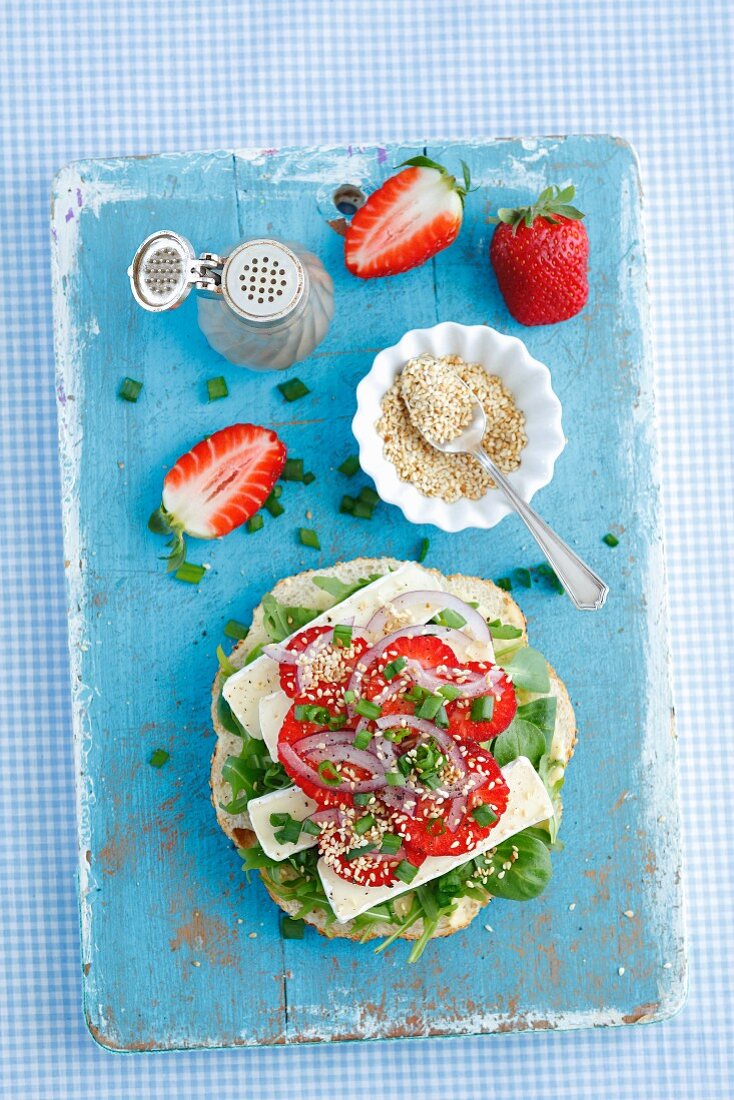 Half a bagel topped with Camembert, red onions and strawberries