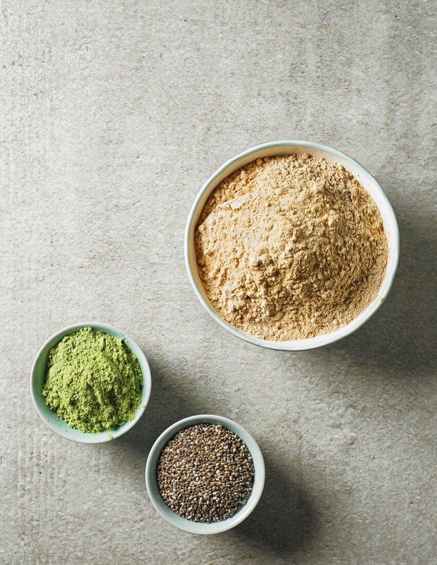 Maca powder, barley sprouts powder and chia seeds in various bowls (seen from above)