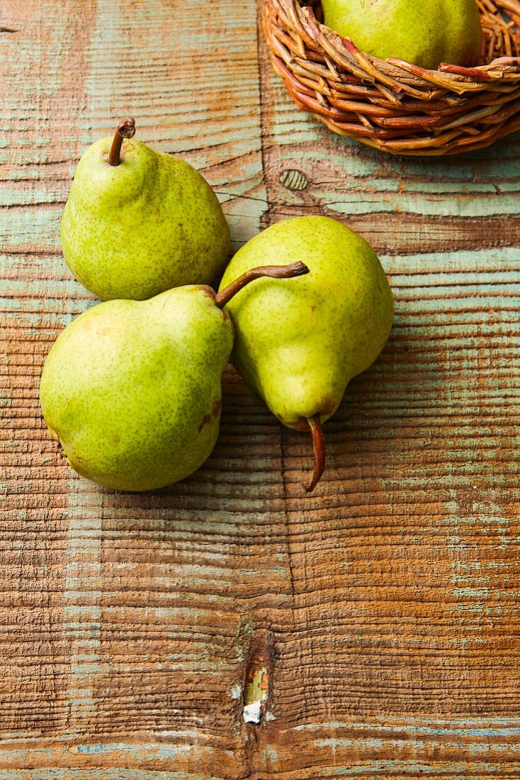 Green pears on a wooden surface and in a basket