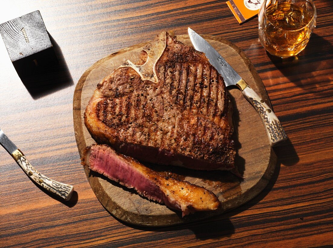 Sliced grilled T-bone steak on a wooden plate with a steak knife