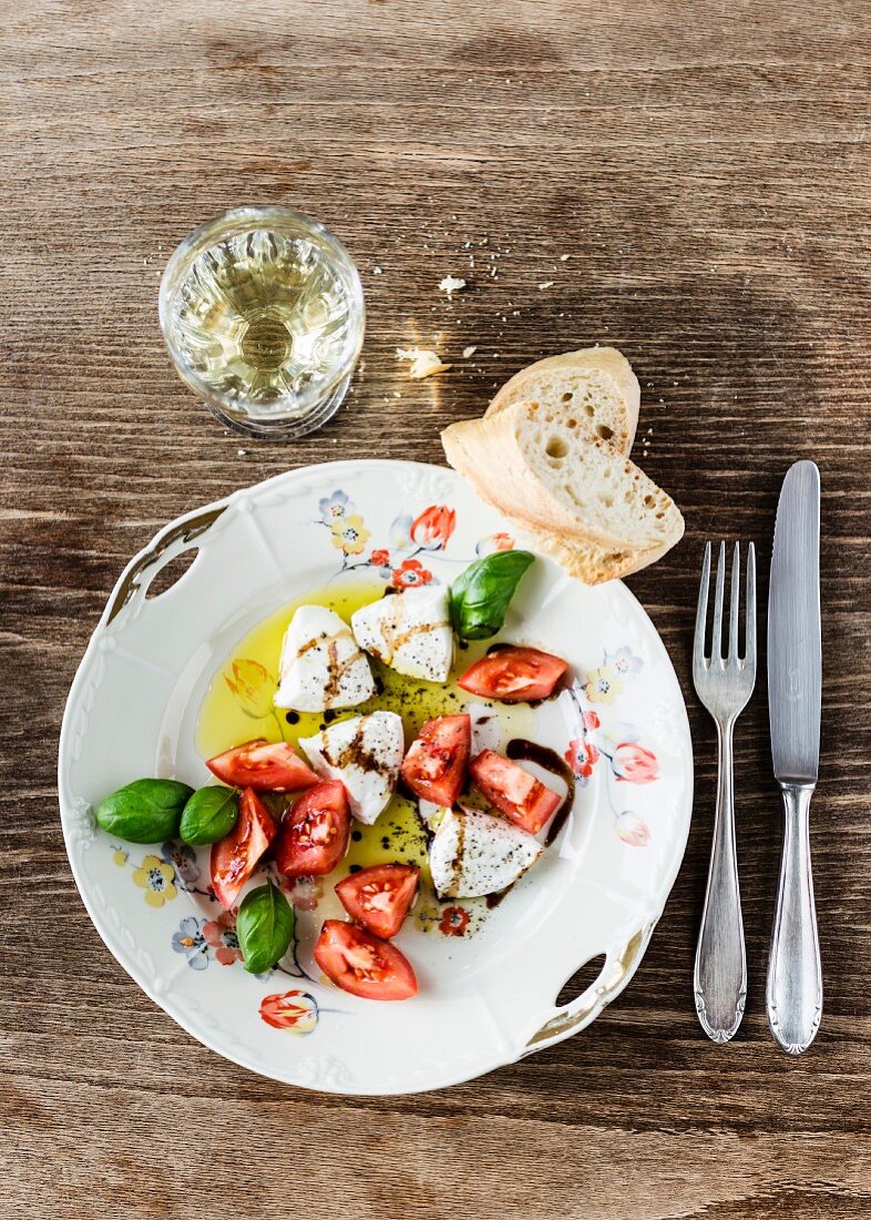 Mozzarella, Tomatenstücke, Basilikum und Baguette mit Olivenöl und Balsamico auf altem Porzellanteller mit Blumendekor