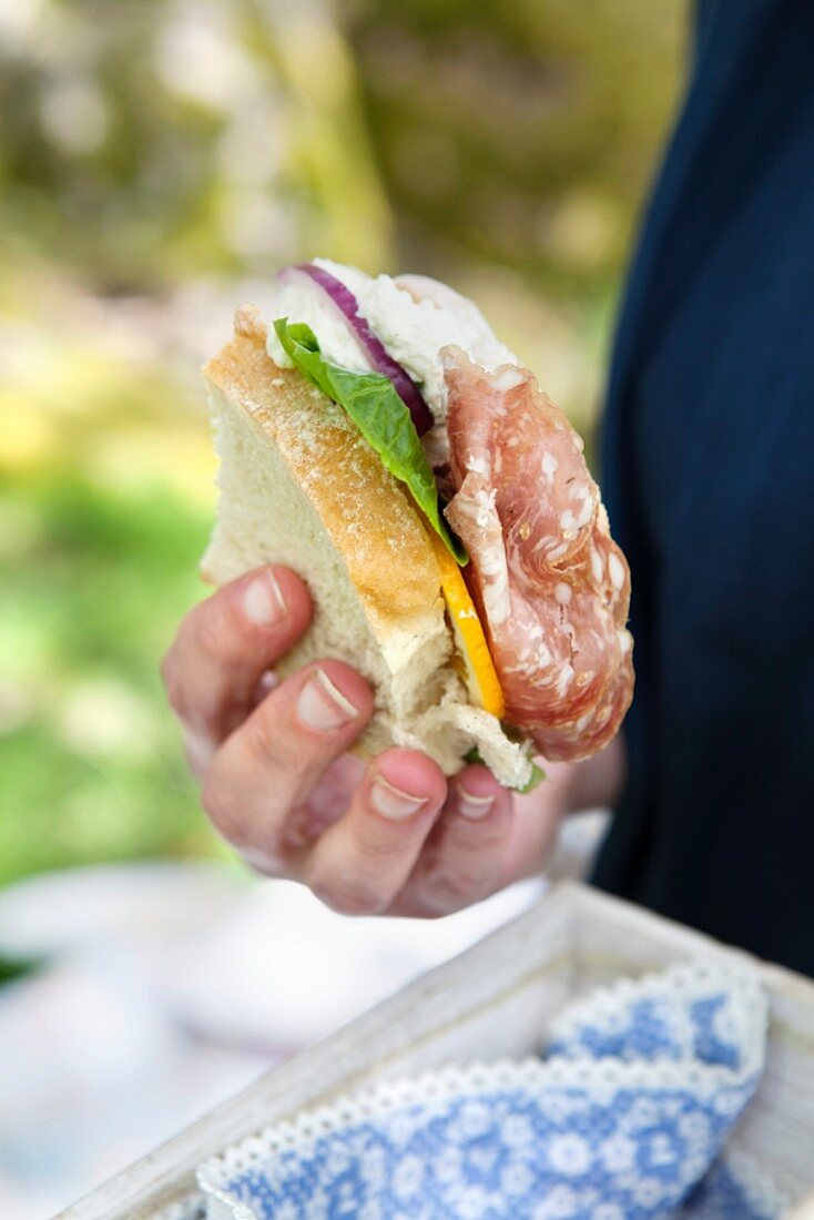 Hand hält Picknick-Sandwich mit Salami und Salat