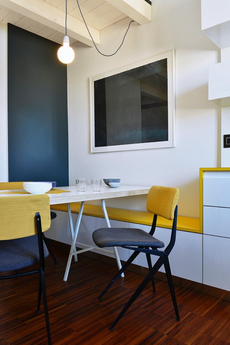 Minimalistischer Esstisch und Stühle vor Wand mit massgefertigter Bank mit gelber Sitzfläche