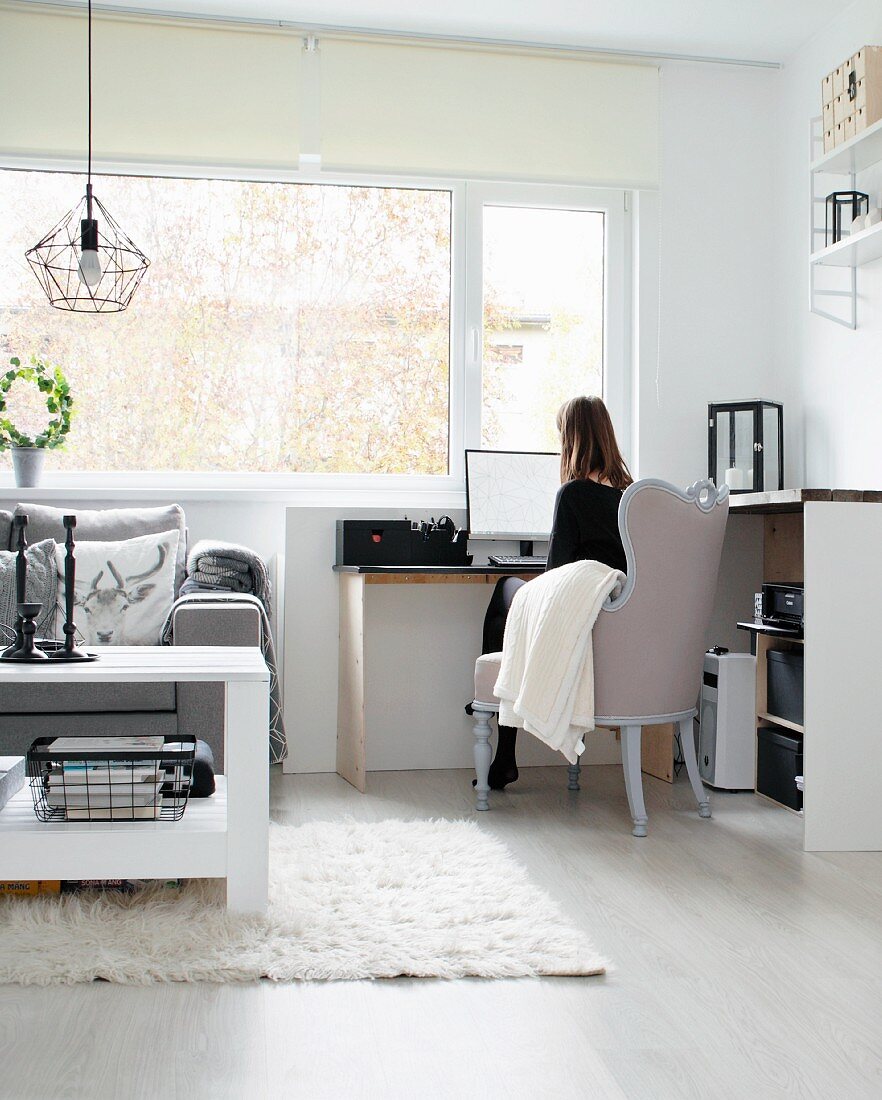 Study area in living room; woman sitting on antique armchair at desk below window