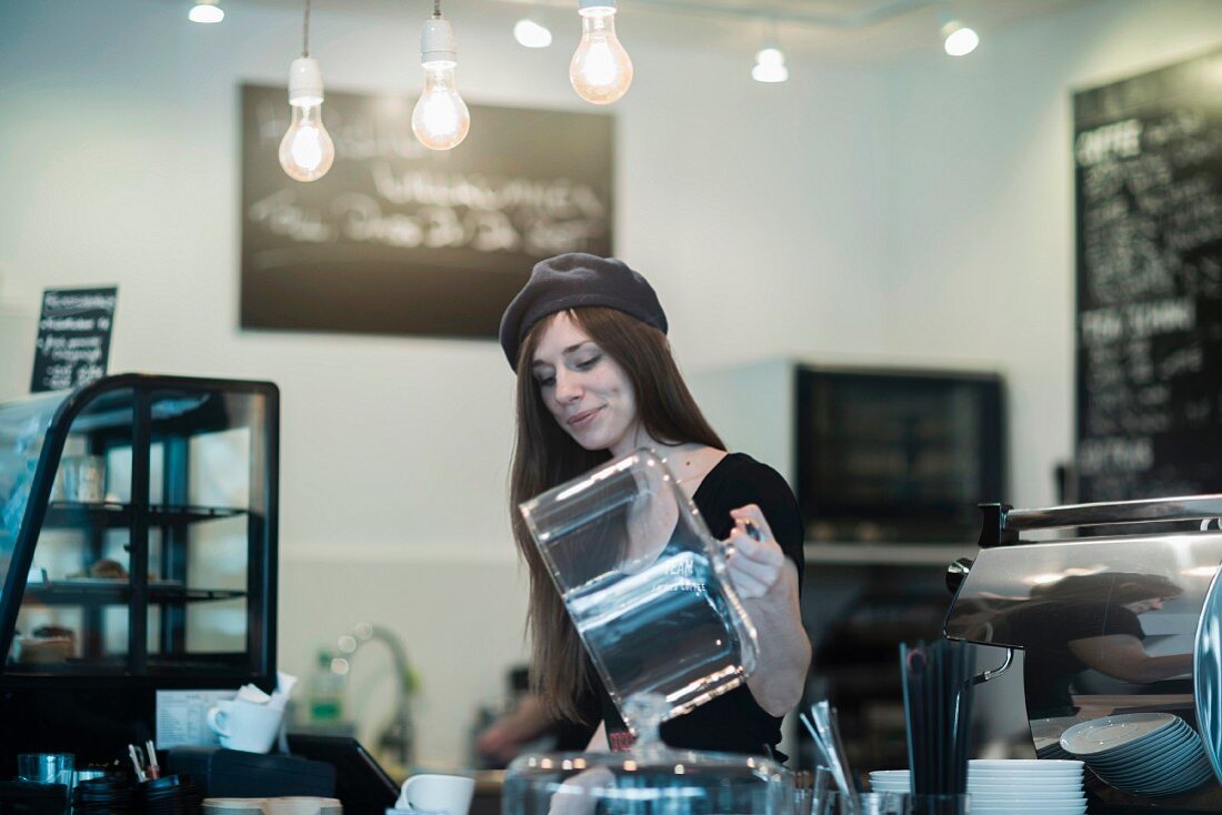 Junge Kellnerin mit Mütze bei der Arbeit in einem Café